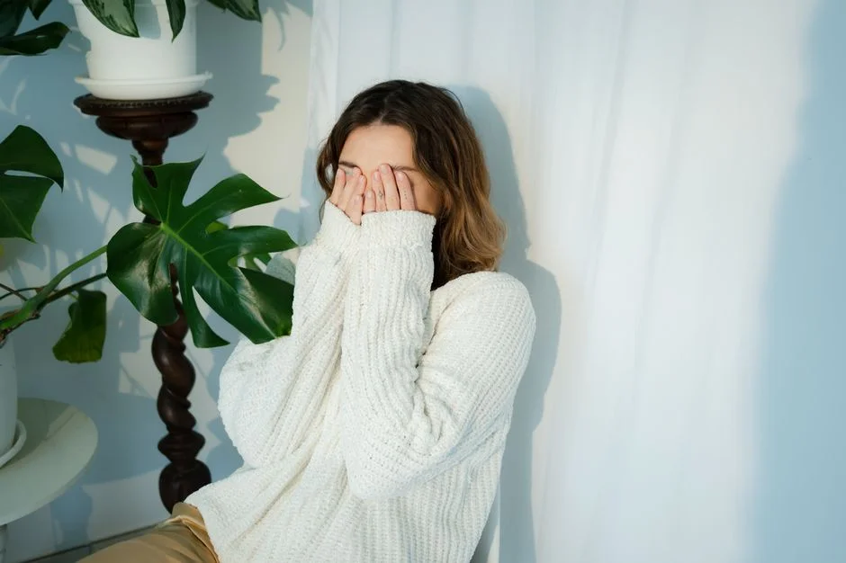 セーターの袖で顔を隠す女性