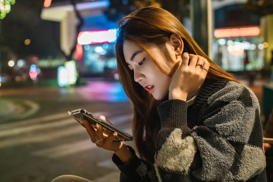 夜にスマートフォンを見て連絡を待つ女性