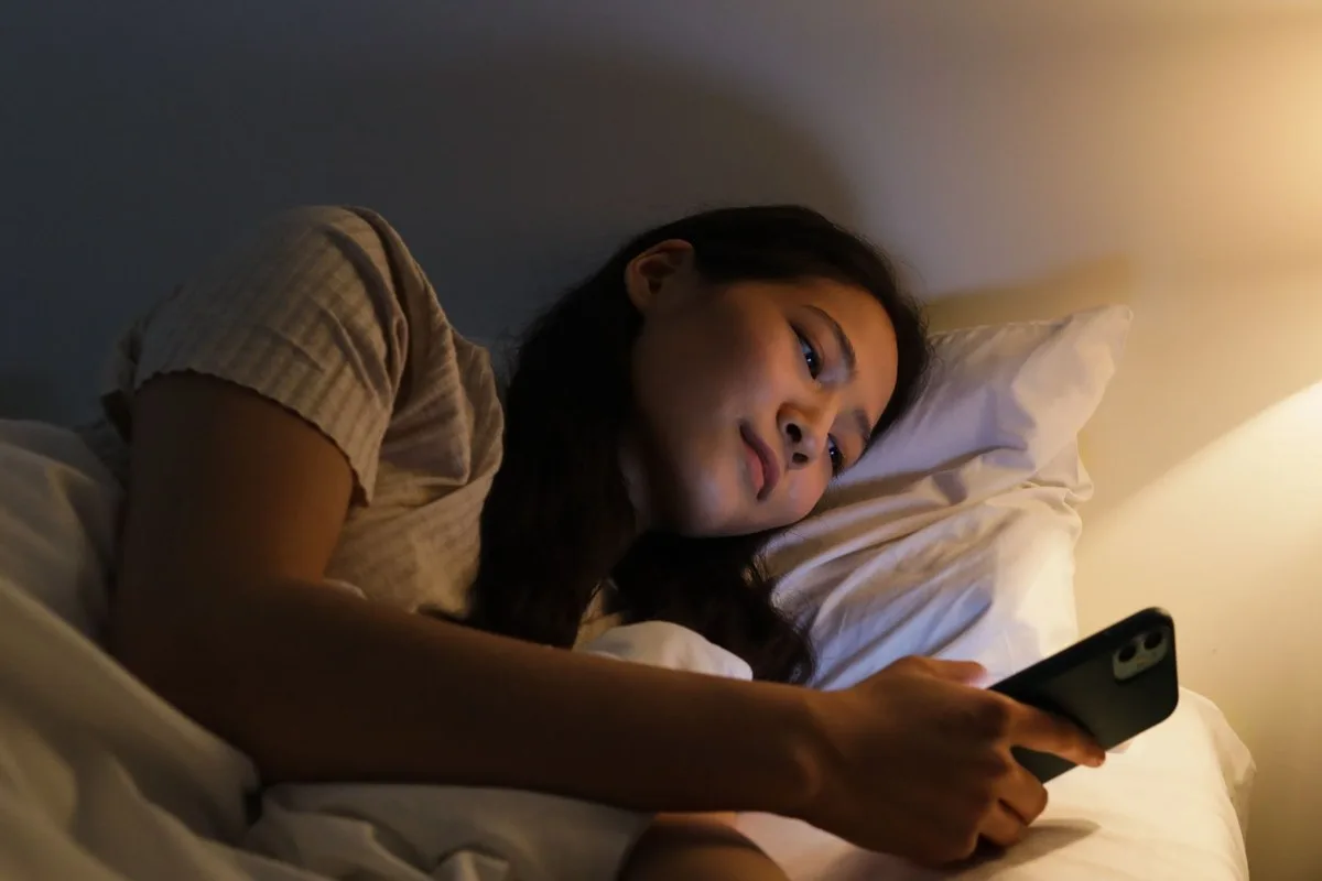 夜の窓辺でスマートフォンを見つめる女性