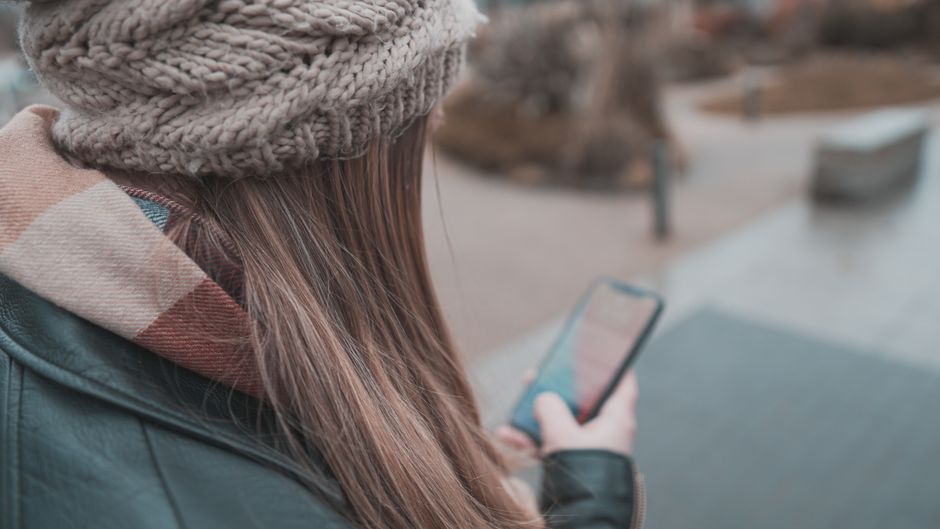 スマートフォンを手にどうするか迷う女性の後ろ姿