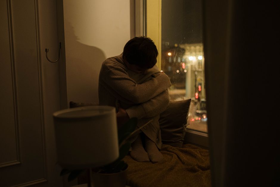 夜、一人で膝を抱えて座る人物の後ろ姿