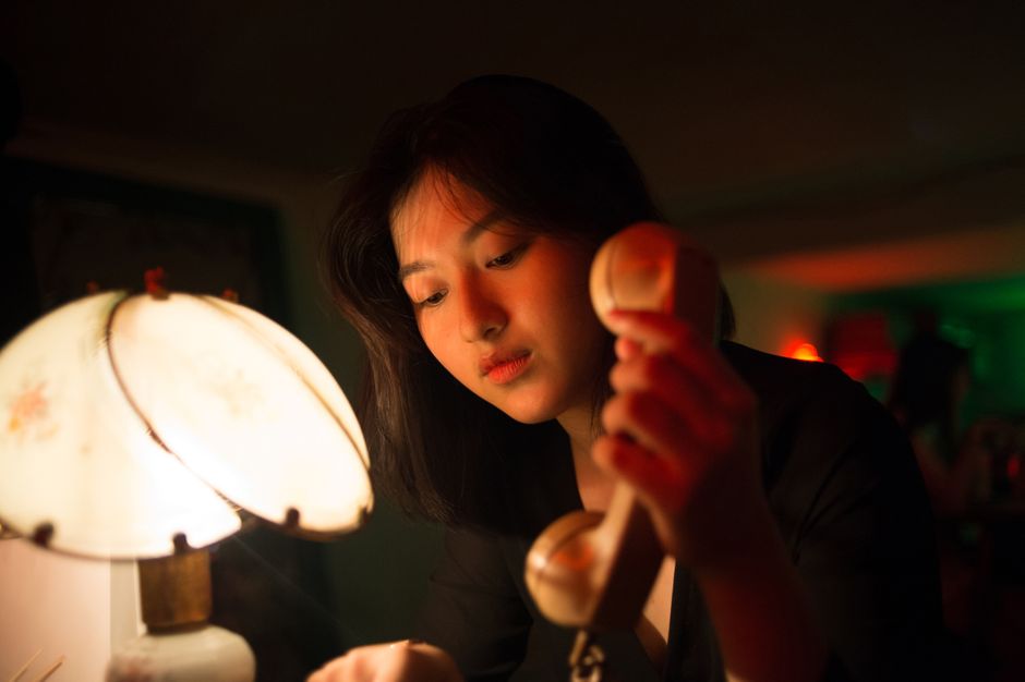 暗い部屋で電話の受話器を見つめる女性