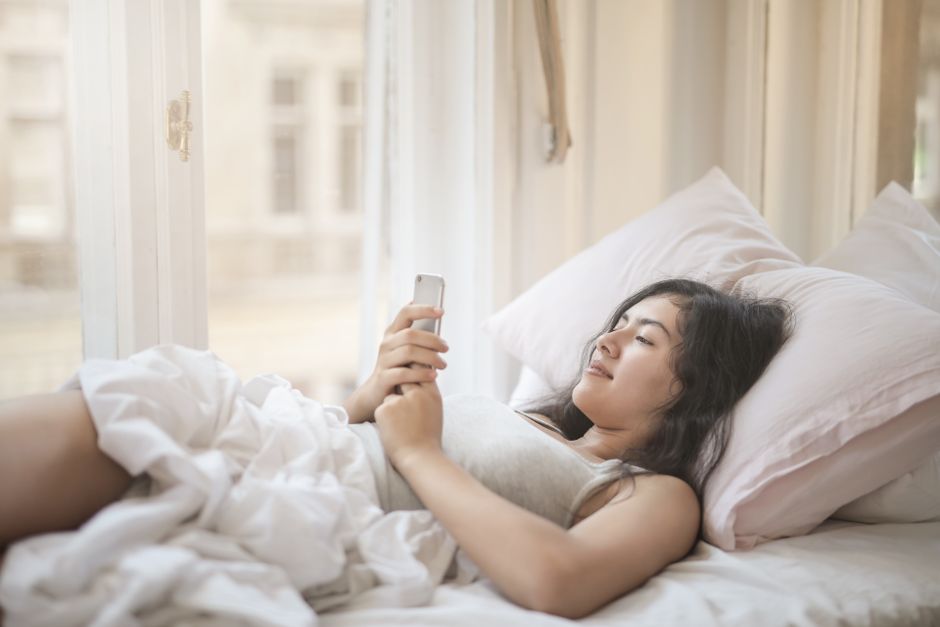 窓辺でスマホの口コミを確認する女性